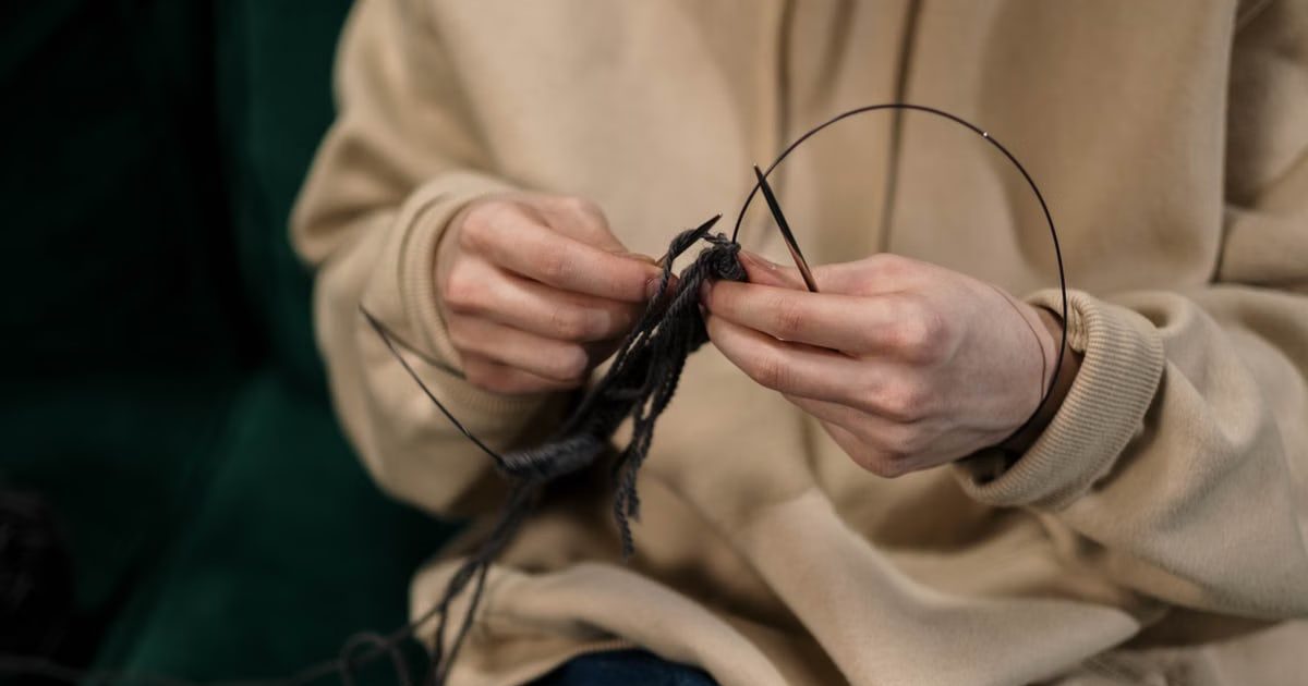 Hands skillfully knitting black yarn, showcasing a cozy indoor hobby.