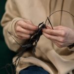 Hands skillfully knitting black yarn, showcasing a cozy indoor hobby.