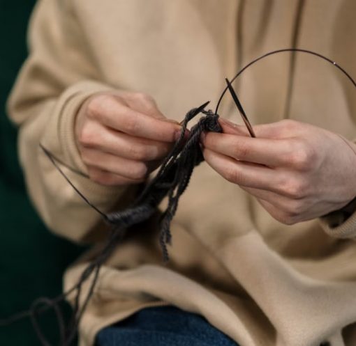 Hands skillfully knitting black yarn, showcasing a cozy indoor hobby.