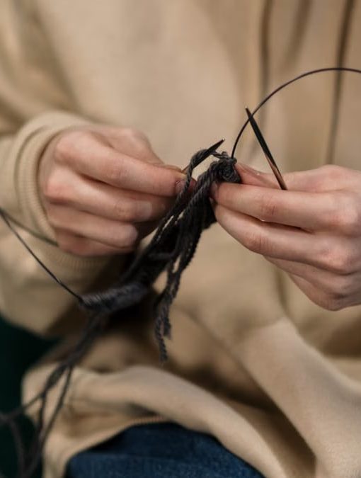 Hands skillfully knitting black yarn, showcasing a cozy indoor hobby.