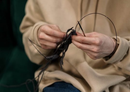 Hands skillfully knitting black yarn, showcasing a cozy indoor hobby.