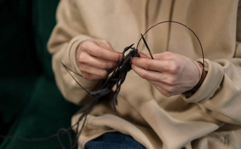 Hands skillfully knitting black yarn, showcasing a cozy indoor hobby.