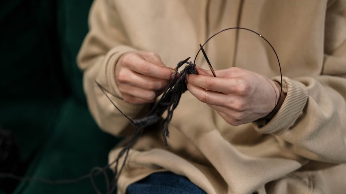 Hands skillfully knitting black yarn, showcasing a cozy indoor hobby.